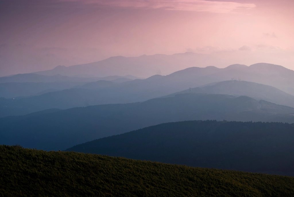 Layers of blue mountain ridges at dusk above a grassy slope